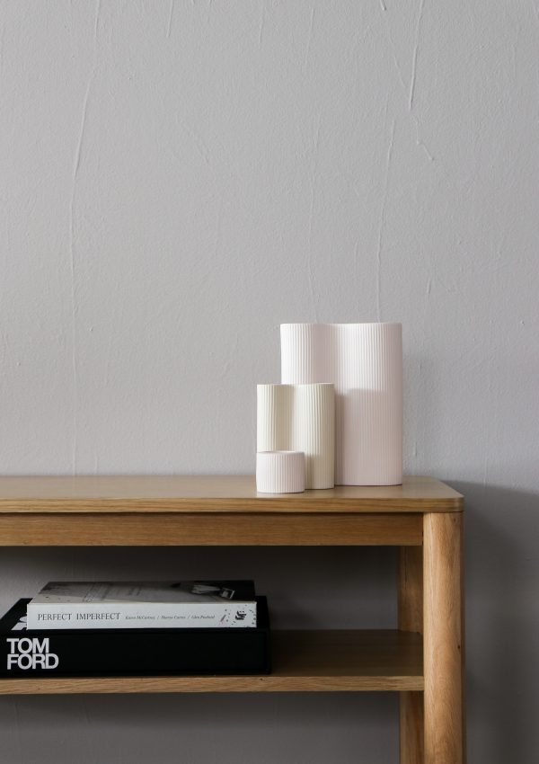 light wood skinny console table with tom ford book and white textured vases